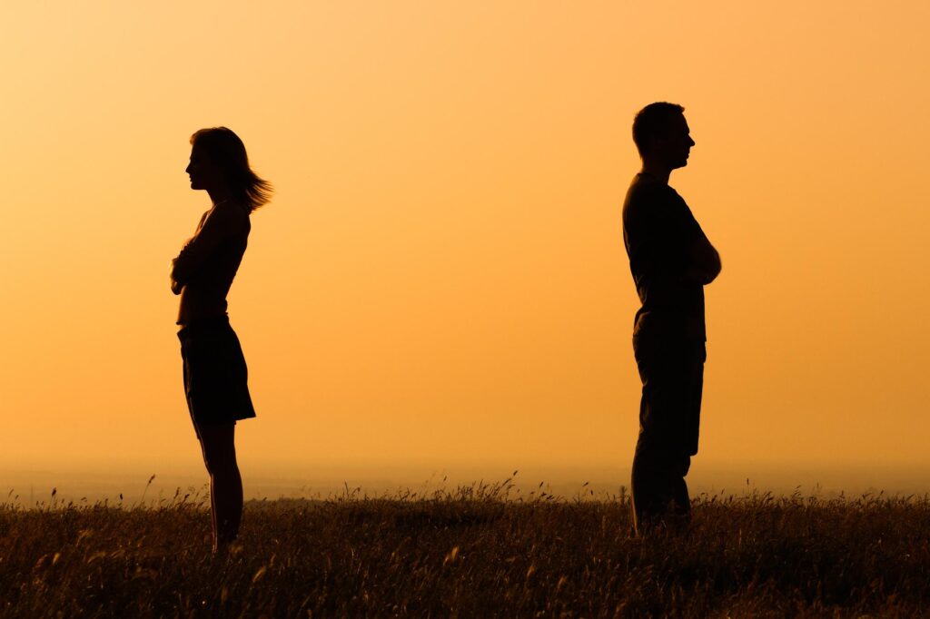 Two people who appear angry with each other. They're standing with their backs to each other with their arms crossed in front of them.