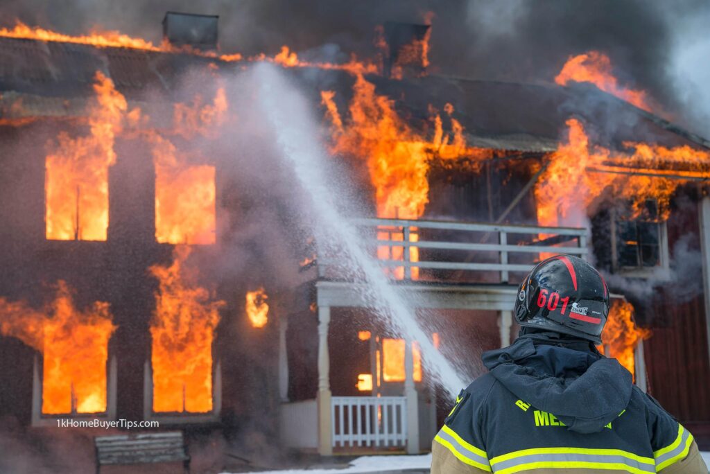 fireman with hose and water pointed to a burning home on fire