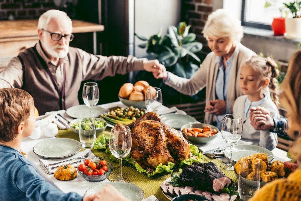 A family gathered around the table for Thanksgiving holding hands in prayer and gratitude