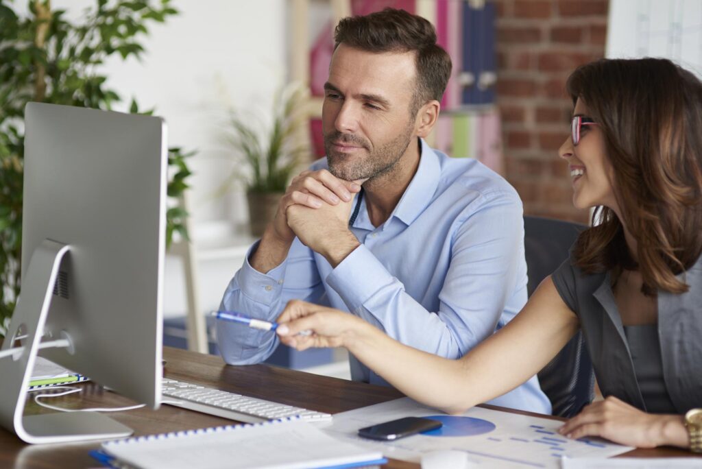 man and woman sitting at computer talking over data